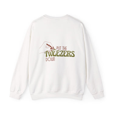 White sweatshirt featuring a humorous graphic with a line art hand, reddish-brown nail polish holding tweezers, and the text Put The Tweezers Down where Tweezers is in a bold green font