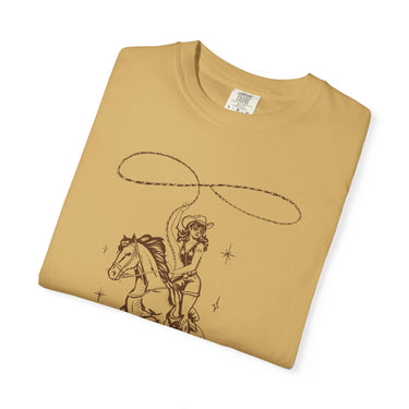 Fawn Comfort Colors t-shirt featuring a brown outline vintage graphic of a pin-up cowgirl in a cowboy hat and sunglasses riding a horse while swinging a lasso