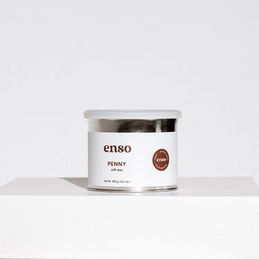 A clear-lidded silver enso PENNY soft wax container with a white label displaying brown enso text and a circular brown sticker highlighting vegan antimicrobial hypoallergenic features on a clean white studio surface