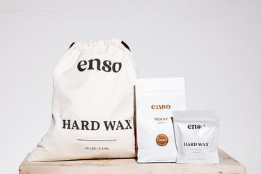 Three Enso Hard Wax products, including a large 10lb canvas bag, a medium 1kg Penny pouch with a brown vegan antimicrobial hypoallergenic label, and a small 5oz sample pouch, displayed on a light wooden surface
