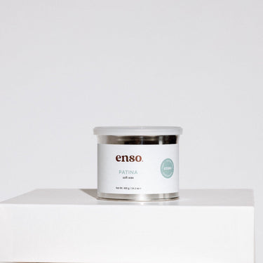 Product photograph of enso PATINA soft wax in a silver metallic container resting on a white pedestal, featuring a white label with black branding, a round light green vegan and hypoallergenic sticker, and a clear plastic lid